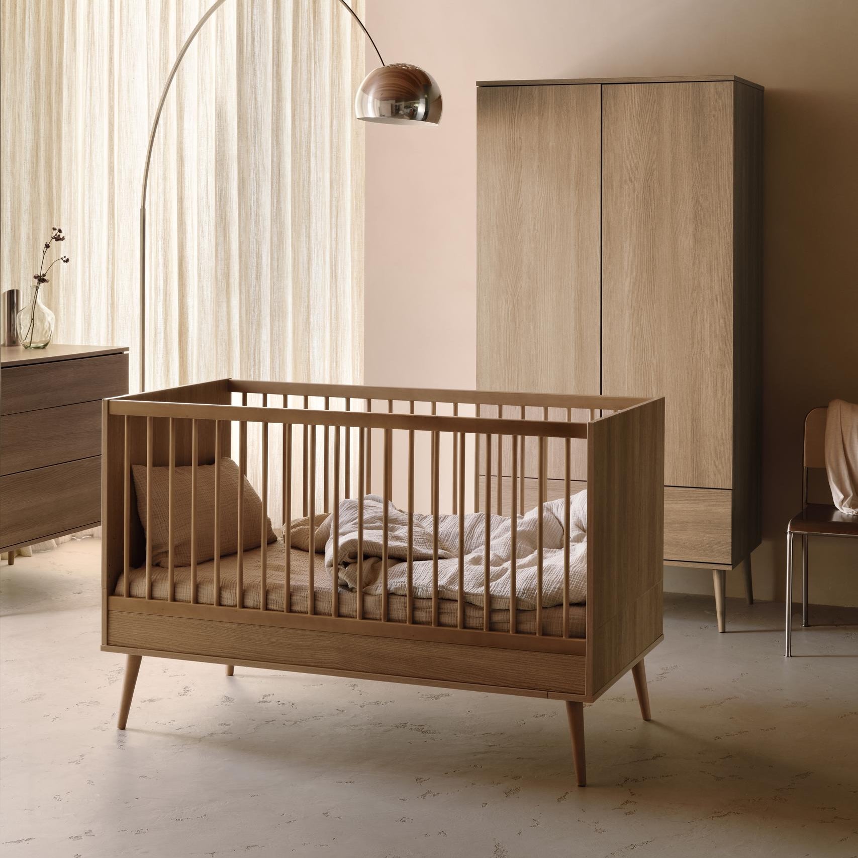 Quax Flow cot bed in honey ash styled in a modern nursery with matching wardrobe and floor lamp