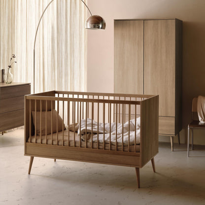Quax Flow cot bed in honey ash styled in a modern nursery with matching wardrobe and floor lamp