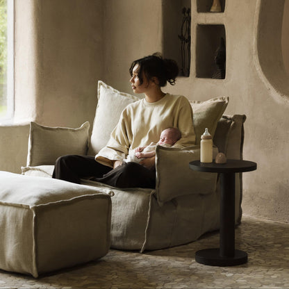 Woman sitting on a couch holding a baby in a cozy room with neutral tones.
