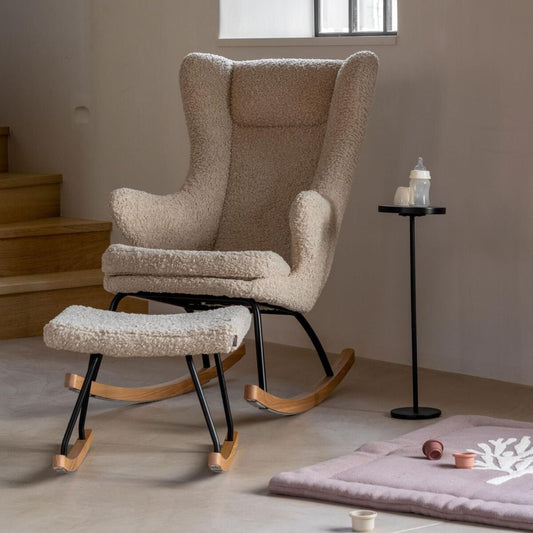 Beige nursing armchair with ottoman in a room with a window and small table.