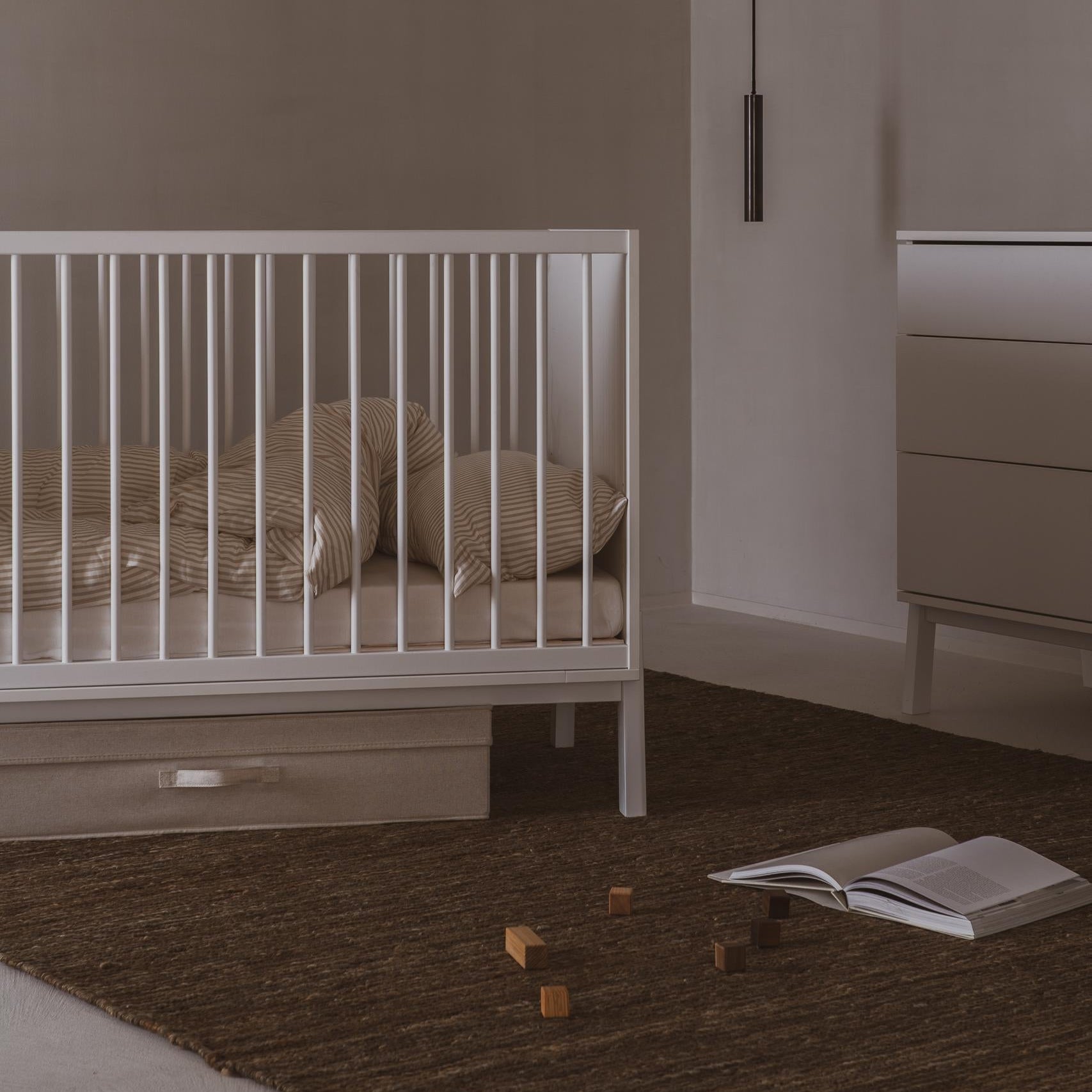 Nursery room with a crib, dresser, and open book on the floor.