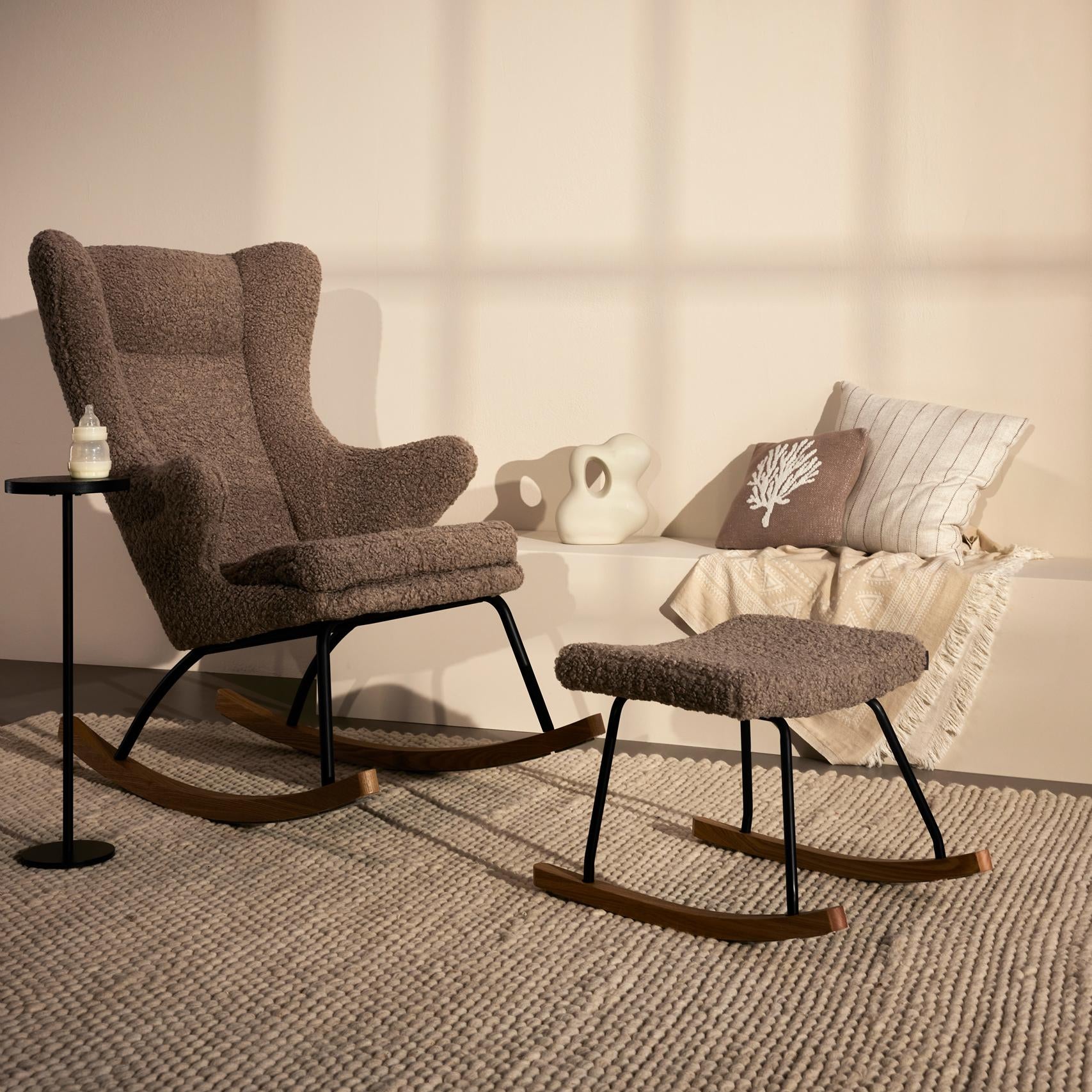 Brown nursing rocking chair with ottoman in a room with light-colored walls and rug.