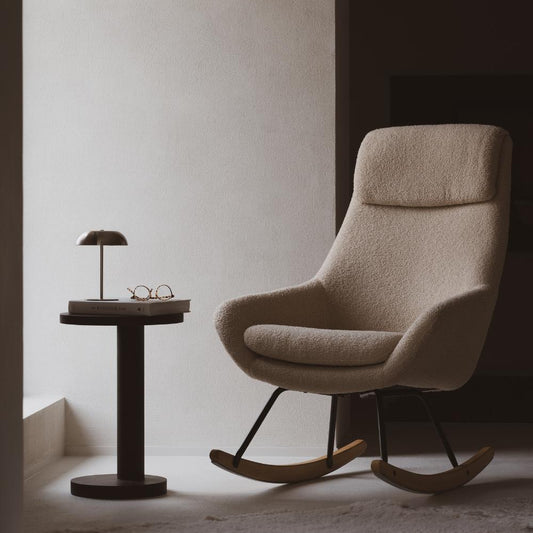 Beige rocking chair in a minimalistic room with a side table and lamp.