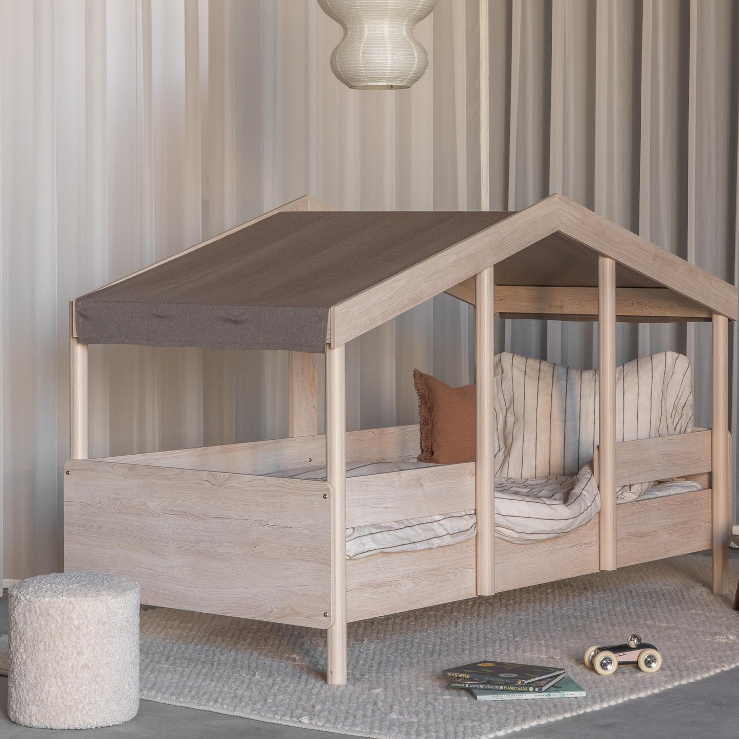 Children's montessori house-shaped bed with wooden frame and brown roof in a room setting.