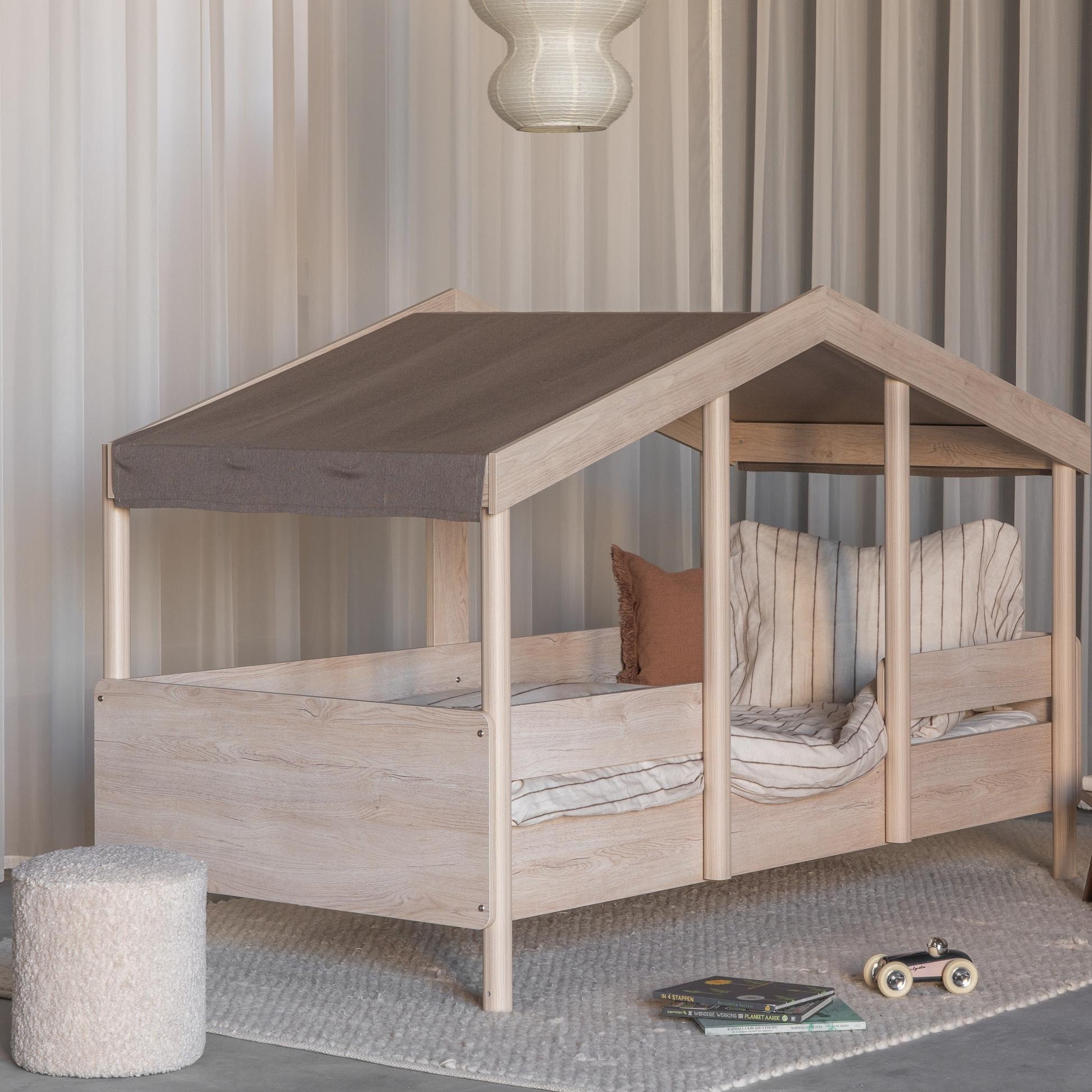 Children's montessori house-shaped bed with wooden frame and brown roof in a room setting.