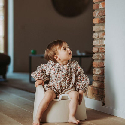 Child sitting on a potty in a room with wooden flooring and a brick wall.