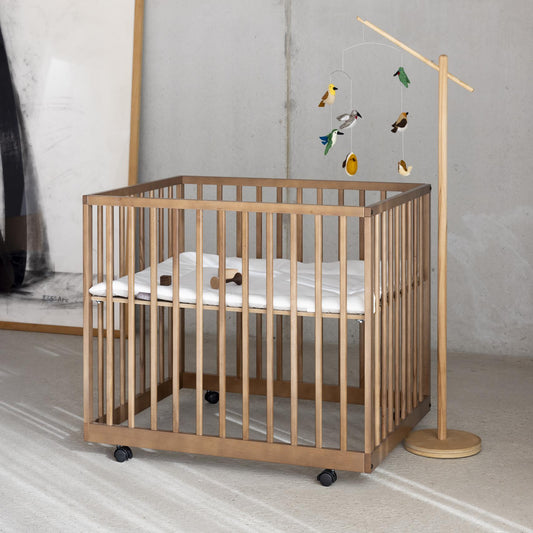Wooden crib with a baby mobile in a minimalistic room.