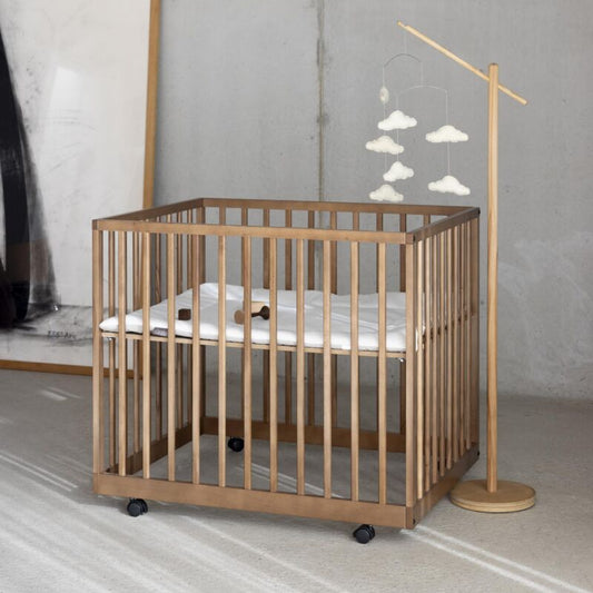 Wooden crib with white mattress in a minimalistic room with a lamp and abstract wall art.
