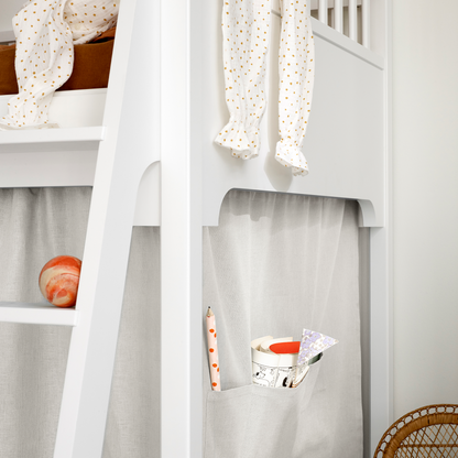 White loft bed with curtains and a small table with items on it.