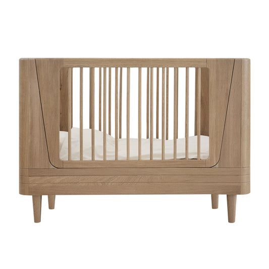 Wooden crib with white mattress on a white background