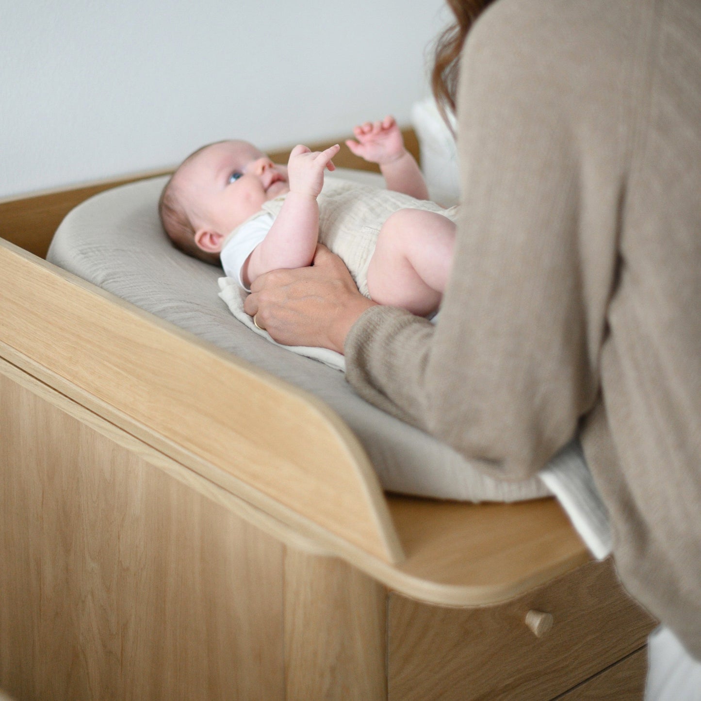 Woman changing a baby on a wooden changing table with a neutral background