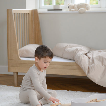 Child playing with toys on the floor in a bedroom with a crib and window in the background.