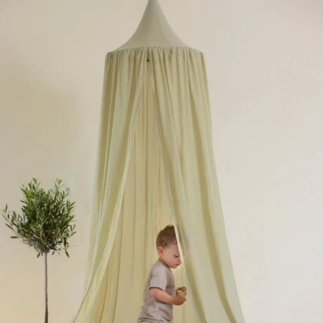 Child playing under a green canopy in a room with a plant and pillows.