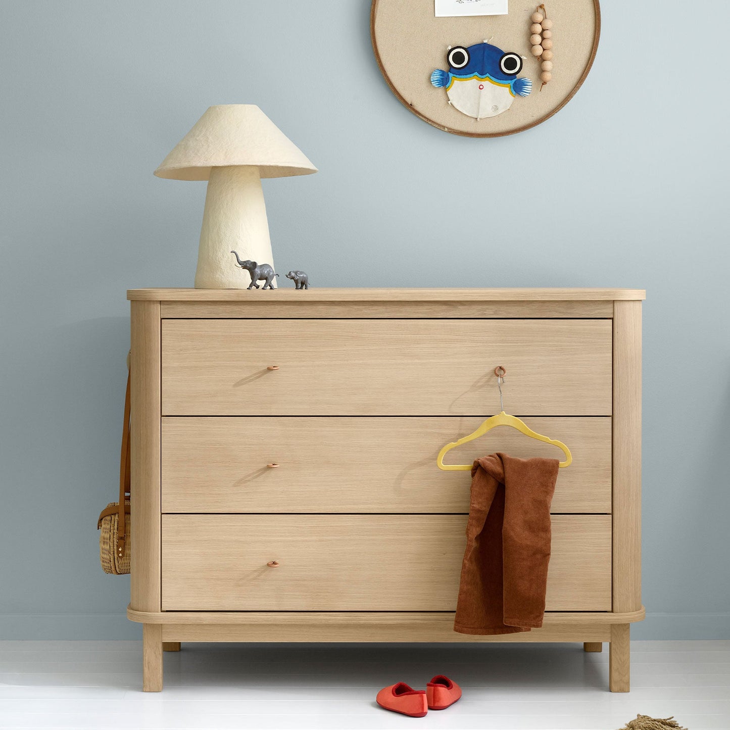 Wooden dresser with a lamp, hanger, and small items against a light blue wall.