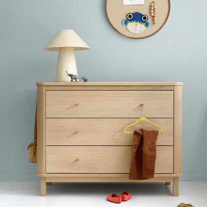 Wooden dresser with a lamp, hanger, and small items against a light blue wall.