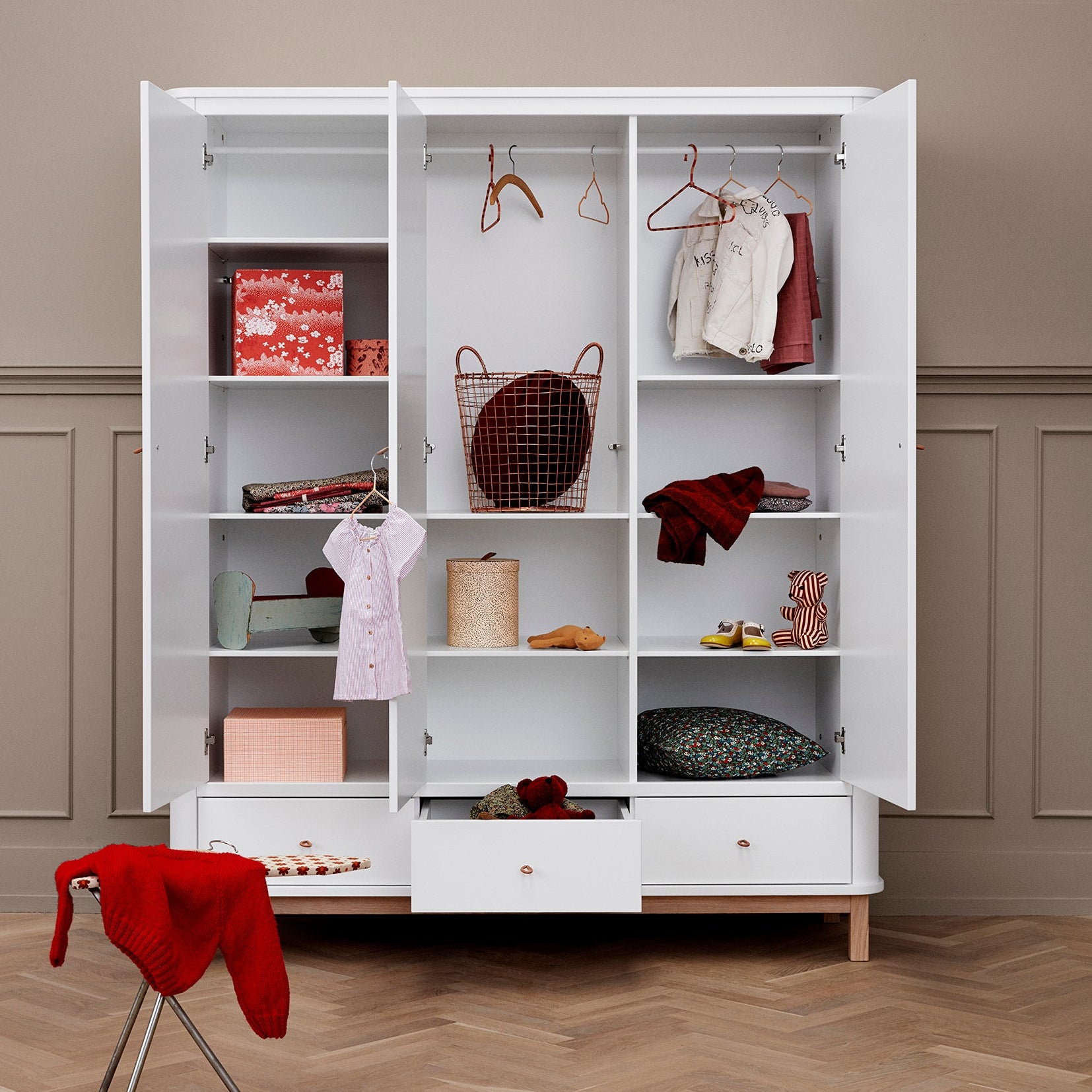 White wardrobe with open doors displaying clothes and items on a wooden floor.