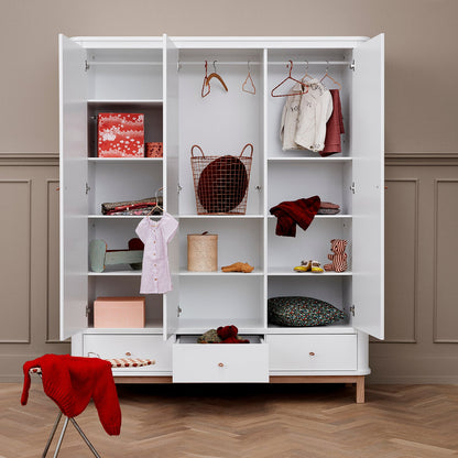 White wardrobe with open doors displaying clothes and items on a wooden floor.