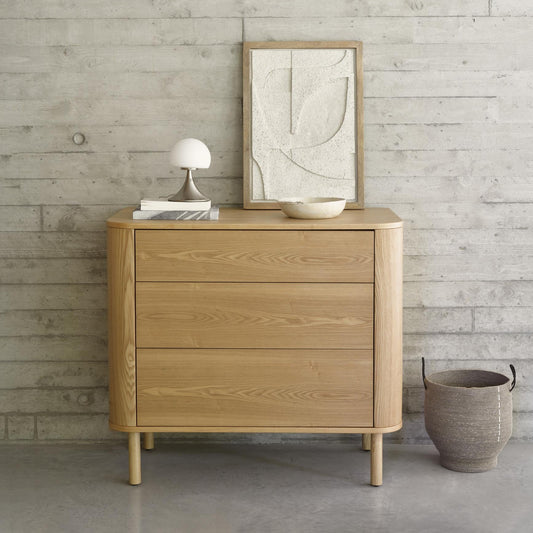 Wooden dresser with decor items against a light wood paneled wall.